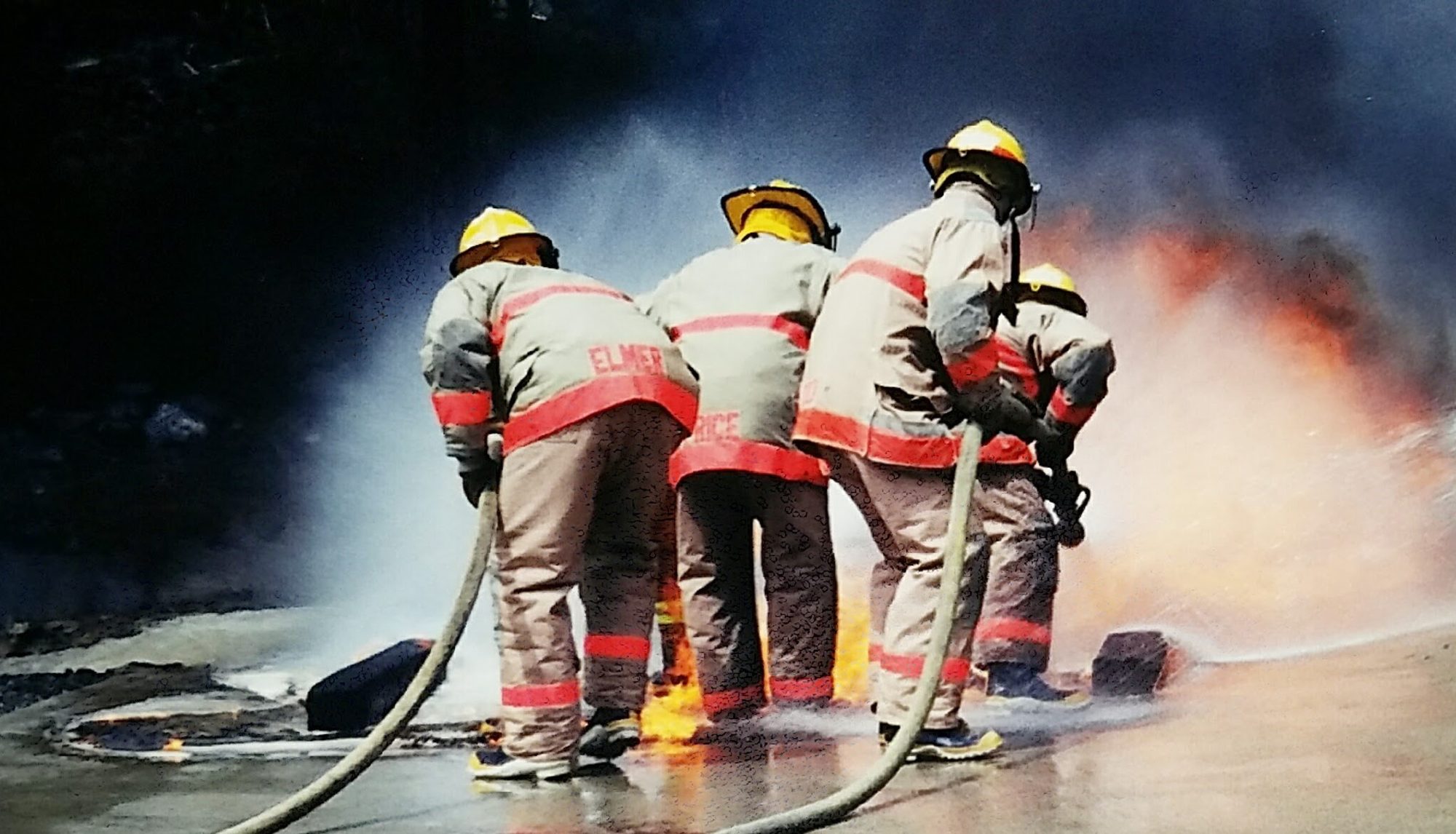 Firefighting crew working a hoseline through smoke and flame